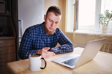 Ofiste cama tabloda, dizüstü bilgisayar ve akıllı telefon kullanan adam.