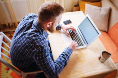 Ofiste net sörf. Dizüstü bilgisayarda çalışan ve Office çalışma evinde otururken gülümseyen kendine güvenen genç adam.