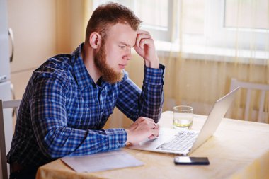 Evde dizüstü bilgisayarda çalışan genç adam..