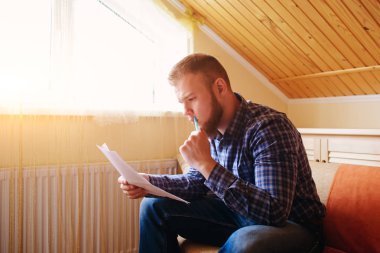 Genç yakışıklı adam kanepede oturan ve bir çalışma kağıdı saatler.