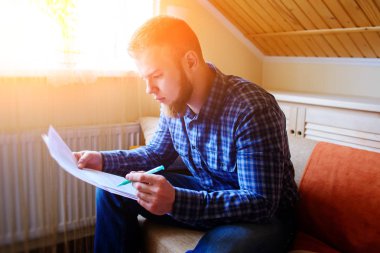 Genç yakışıklı adam kanepede oturan ve bir çalışma kağıdı saatler.