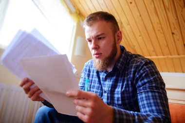 Genç yakışıklı adam kanepede oturan ve bir çalışma kağıdı saatler.