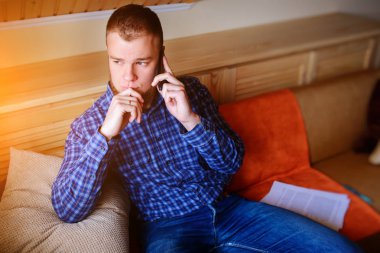 Genç ciddi adam evde kanepede rahat oturan onun telefonda konuşuyor.