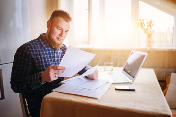 Businessman at home, he is working with a laptop, checking paperwork and bills.