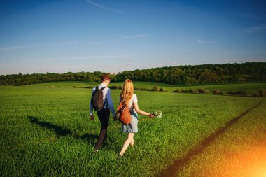 Bir sırt çantası ile bir adam bir şapka ve uzun saçlı bir kadın yol boyunca gidin. Çayır boyunca birkaç yürür.