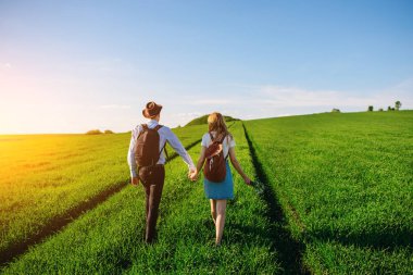 Bir sırt çantası ile bir adam bir şapka ve uzun saçlı bir kadın yol boyunca gidin. Çayır boyunca birkaç yürür.