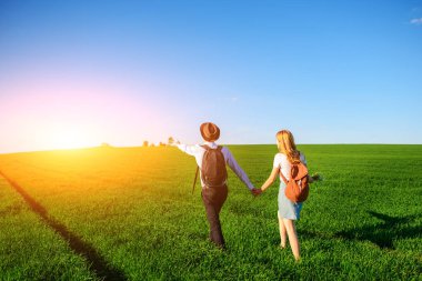 Bir sırt çantası ile bir adam bir şapka ve uzun saçlı bir kadın yol boyunca gidin. Çayır boyunca birkaç yürür.