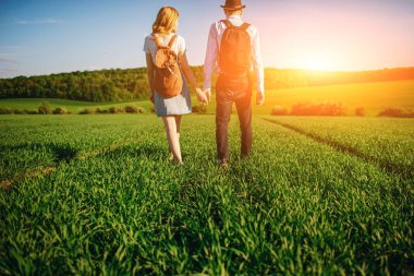 Bir sırt çantası ile bir adam bir şapka ve uzun saçlı bir kadın yol boyunca gidin. Çayır boyunca birkaç yürür.