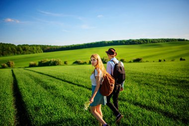 Bir sırt çantası ile bir adam bir şapka ve uzun saçlı bir kadın yol boyunca gidin. Çayır boyunca birkaç yürür.