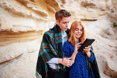 Güzel kadın ve yakışıklı bir battaniyeye sarılmış. Onlar gülümseyen ve bir tablet ekranında bir kum ocağı arka plan üzerinde seyir.
