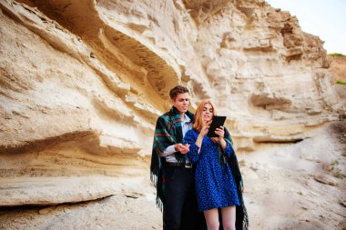 Güzel kadın ve yakışıklı bir battaniyeye sarılmış. Onlar gülümseyen ve bir tablet ekranında bir kum ocağı arka plan üzerinde seyir.