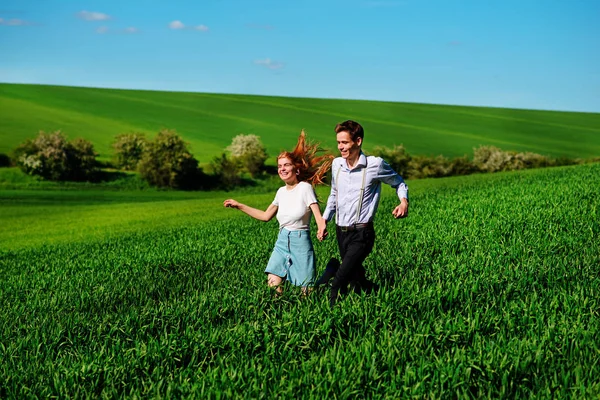 年轻的快乐恋人在草甸与绿草和蓝蓝的天空上运行 — 图库照片