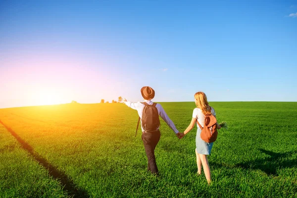 Bir sırt çantası ile bir adam bir şapka ve uzun saçlı bir kadın yol boyunca gidin. Çayır boyunca birkaç yürür.