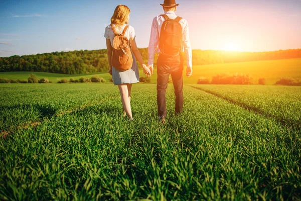 Bir sırt çantası ile bir adam bir şapka ve uzun saçlı bir kadın yol boyunca gidin. Çayır boyunca birkaç yürür.