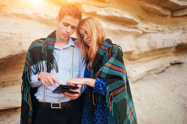 Güzel kadın ve yakışıklı bir battaniyeye sarılmış. Onlar gülümseyen ve bir tablet ekranında bir kum ocağı arka plan üzerinde seyir.