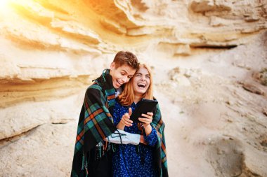 Güzel kadın ve yakışıklı bir battaniyeye sarılmış. Onlar gülümseyen ve bir tablet ekranında bir kum ocağı arka plan üzerinde seyir.