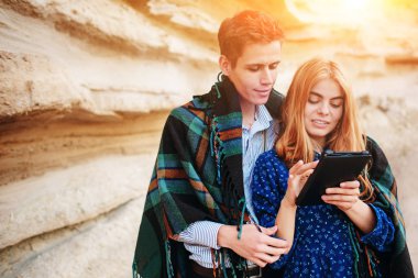 Güzel kadın ve yakışıklı bir battaniyeye sarılmış. Onlar gülümseyen ve bir tablet ekranında bir kum ocağı arka plan üzerinde seyir.