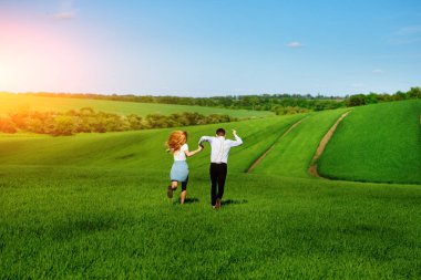 Mutlu aşıklar çayır yeşil çim ve arkasından mavi gökyüzü ile çalışan.