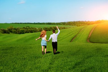 Mutlu aşıklar çayır yeşil çim ve arkasından mavi gökyüzü ile çalışan.