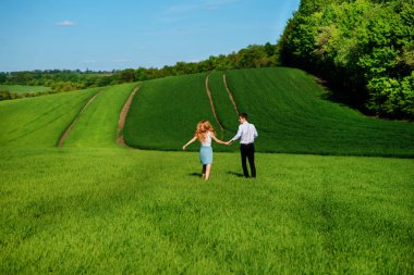 Mutlu aşıklar çayır yeşil çim ve arkasından mavi gökyüzü ile çalışan.