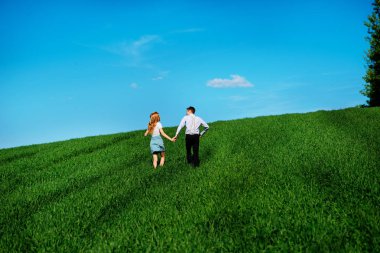 Mutlu aşıklar çayır yeşil çim ve arkasından mavi gökyüzü ile çalışan.