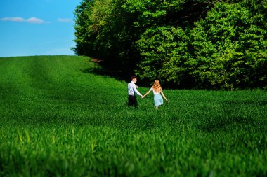 Mutlu aşıklar çayır yeşil çim ve arkasından mavi gökyüzü ile çalışan.
