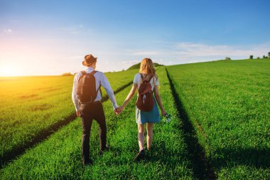 Bir sırt çantası ile bir adam bir şapka ve uzun saçlı bir kadın yol boyunca gidin. Çayır boyunca birkaç yürür.