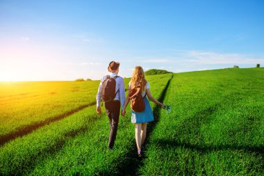 Bir sırt çantası ile bir adam bir şapka ve uzun saçlı bir kadın yol boyunca gidin. Çayır boyunca birkaç yürür.