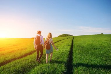 Bir sırt çantası ile bir adam bir şapka ve uzun saçlı bir kadın yol boyunca gidin. Çayır boyunca birkaç yürür.