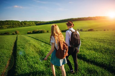 Bir sırt çantası ile bir adam bir şapka ve uzun saçlı bir kadın yol boyunca gidin. Çayır boyunca birkaç yürür.