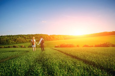 Bir sırt çantası ile bir adam bir şapka ve uzun saçlı bir kadın yol boyunca gidin. Çayır boyunca birkaç yürür.