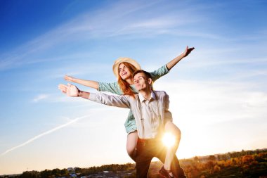 Genç adam neşeli kız arkadaş gibi gökyüzü arka plan üzerinde uçak piggybacking.