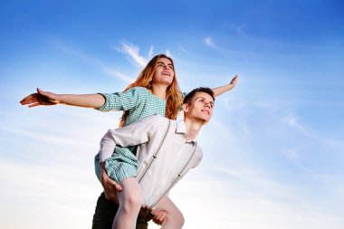 Genç adam neşeli kız arkadaş gibi gökyüzü arka plan üzerinde uçak piggybacking.