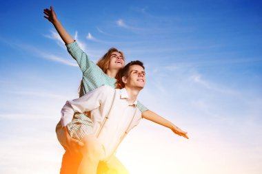 Genç adam neşeli kız arkadaş gibi gökyüzü arka plan üzerinde uçak piggybacking.