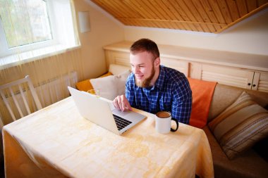 Onun laptop içinde internette sörf rahat genç profesyonel bir yemek odası.