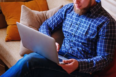 Genç adam sahilde bilgisayarla çalışma. Yakışıklı adam kanepede plajda döşeme dizüstü bilgisayar ile çalışma.