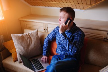 Onun smartphone kullanarak çevrimiçi bankacılık-sıçrama laptop ile kanepede oturan genç adam.