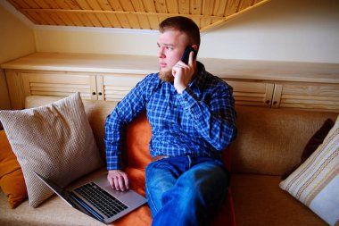 Onun smartphone kullanarak çevrimiçi bankacılık-sıçrama laptop ile kanepede oturan genç adam.