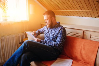 Genç yakışıklı adam kanepede oturan ve bir çalışma kağıdı saatler.