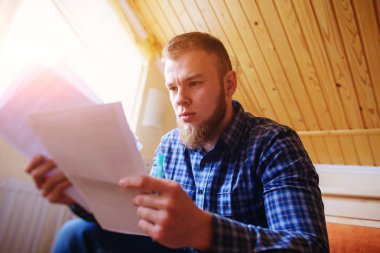 Genç yakışıklı adam kanepede oturan ve bir çalışma kağıdı saatler.