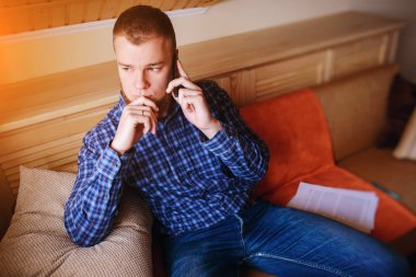 Genç ciddi adam evde kanepede rahat oturan onun telefonda konuşuyor.