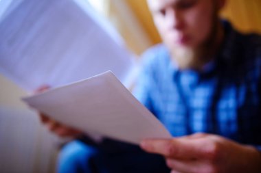 Genç yakışıklı adam kanepede oturan ve bir çalışma kağıdı saatler.