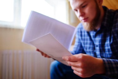 Genç yakışıklı adam kanepede oturan ve bir çalışma kağıdı saatler.