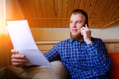 Kağıt basılı tutup evde kanepede otururken cep telefonda konuşurken ciddi olgun adam