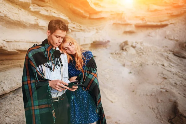 Güzel kadın ve yakışıklı bir battaniyeye sarılmış. Onlar gülümseyen ve bir tablet ekranında bir kum ocağı arka plan üzerinde seyir.