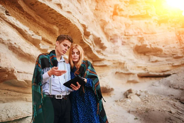 Güzel kadın ve yakışıklı bir battaniyeye sarılmış. Onlar gülümseyen ve bir tablet ekranında bir kum ocağı arka plan üzerinde seyir.