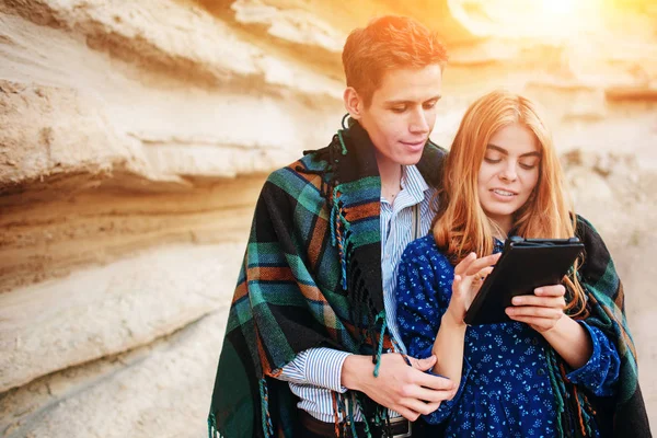 Güzel kadın ve yakışıklı bir battaniyeye sarılmış. Onlar gülümseyen ve bir tablet ekranında bir kum ocağı arka plan üzerinde seyir.