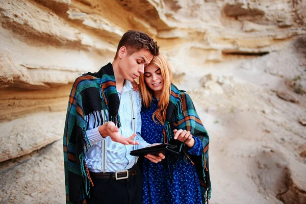 Güzel kadın ve yakışıklı bir battaniyeye sarılmış. Onlar gülümseyen ve bir tablet ekranında bir kum ocağı arka plan üzerinde seyir.