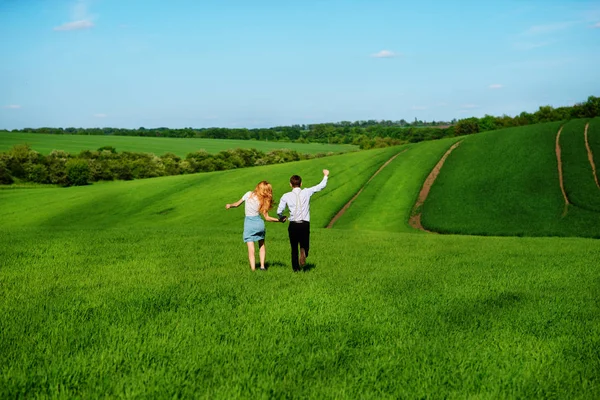 Mutlu aşıklar çayır yeşil çim ve arkasından mavi gökyüzü ile çalışan.