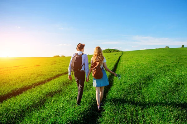 Bir sırt çantası ile bir adam bir şapka ve uzun saçlı bir kadın yol boyunca gidin. Çayır boyunca birkaç yürür.